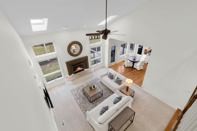 living room with a wealth of natural light, a skylight, a warm lit fireplace, and high vaulted ceiling