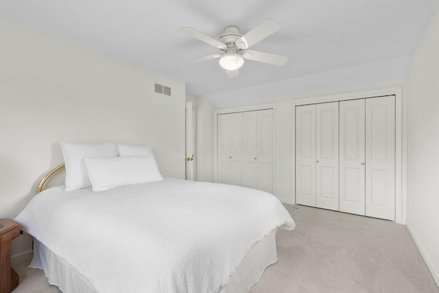 bedroom with visible vents, light colored carpet, two closets, and ceiling fan