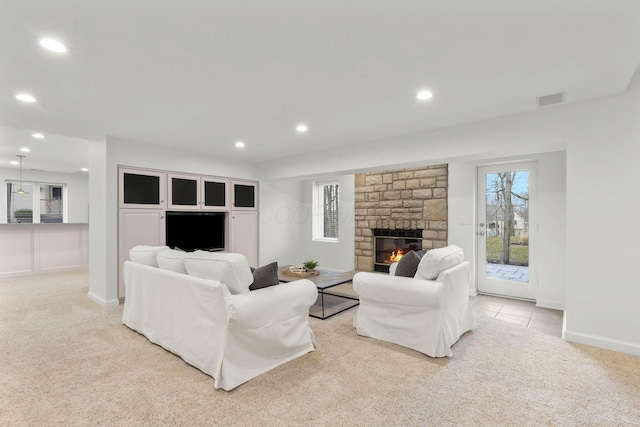 living room with visible vents, light colored carpet, a wealth of natural light, a stone fireplace, and recessed lighting