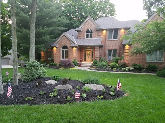 view of front of property featuring brick siding, a front lawn, and roof with shingles