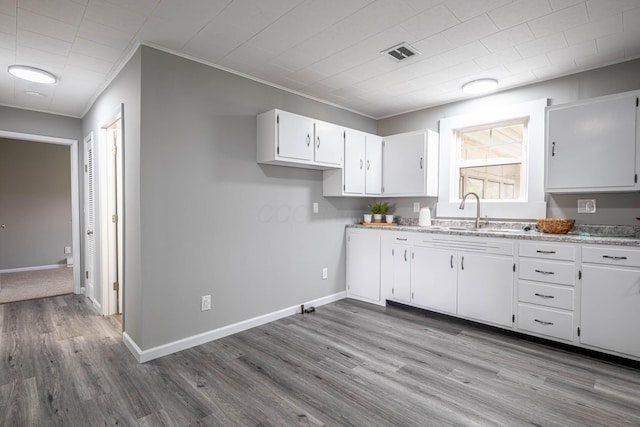 kitchen with white cabinets, baseboards, visible vents, wood finished floors, and ornamental molding