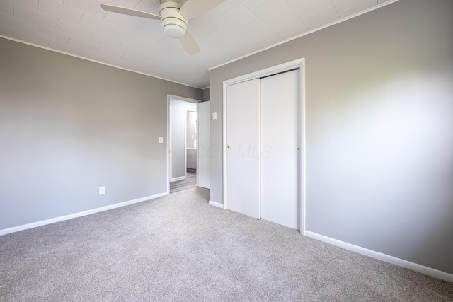 unfurnished bedroom featuring baseboards, a ceiling fan, a closet, crown molding, and carpet floors