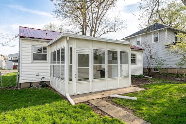 rear view of house with metal roof, a yard, a sunroom, and fence