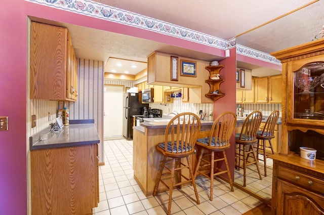 kitchen featuring black refrigerator, a breakfast bar area, light tile patterned floors, kitchen peninsula, and a textured ceiling