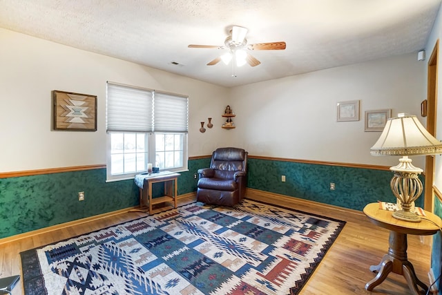 sitting room with ceiling fan, wood-type flooring, and a textured ceiling