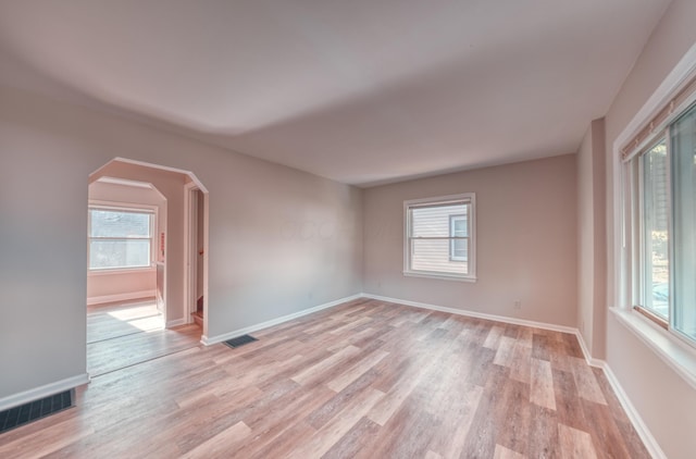 empty room with visible vents, arched walkways, baseboards, and light wood finished floors