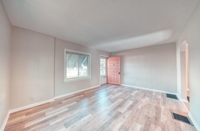 empty room featuring visible vents, arched walkways, baseboards, and light wood-style flooring