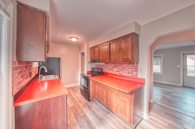 kitchen with under cabinet range hood, light wood-style flooring, brown cabinets, black electric range oven, and a sink