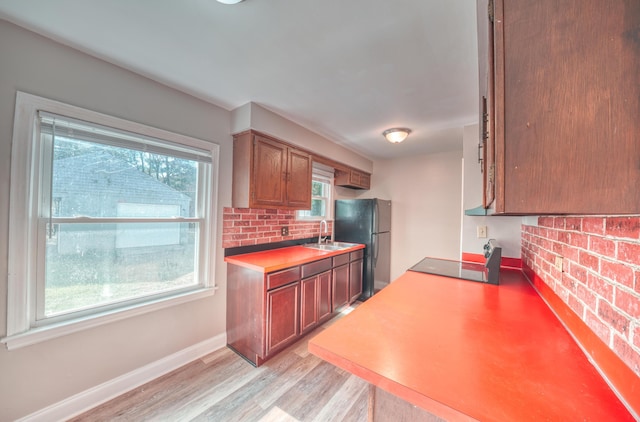 kitchen with tasteful backsplash, brown cabinets, freestanding refrigerator, and a sink