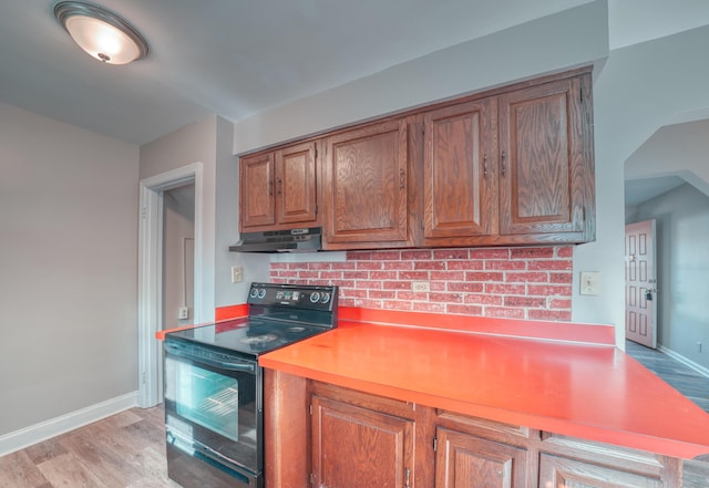 kitchen with brown cabinets, under cabinet range hood, black range with electric cooktop, light wood finished floors, and baseboards