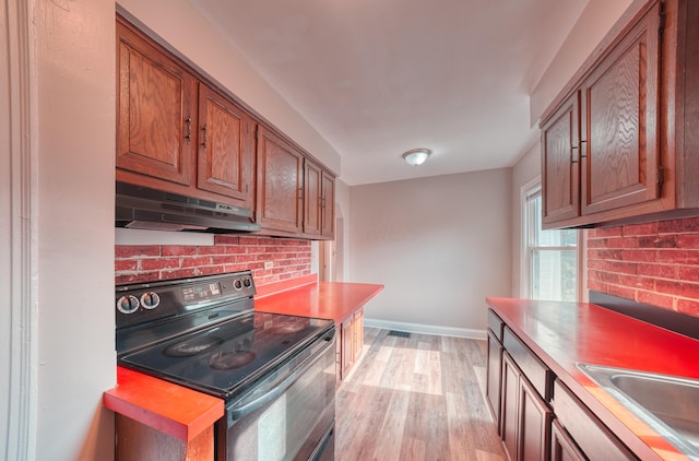 kitchen featuring brown cabinetry, a sink, black electric range, light wood-style floors, and under cabinet range hood