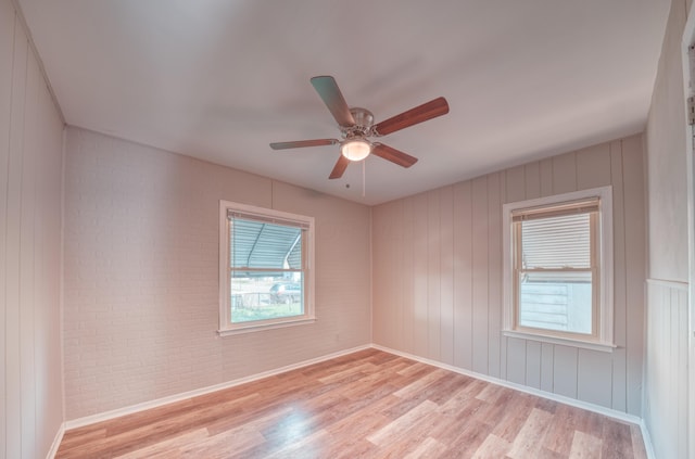 unfurnished room with light wood-style flooring, brick wall, baseboards, and a ceiling fan