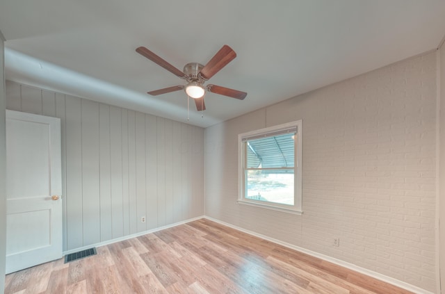 unfurnished room with visible vents, light wood-style flooring, brick wall, baseboards, and ceiling fan