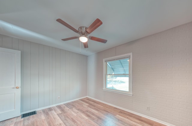 empty room with light wood finished floors, visible vents, brick wall, and a ceiling fan