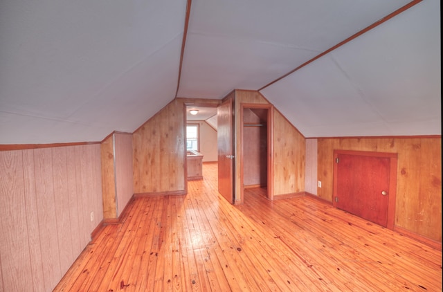 bonus room with light wood-style flooring, wood walls, and vaulted ceiling