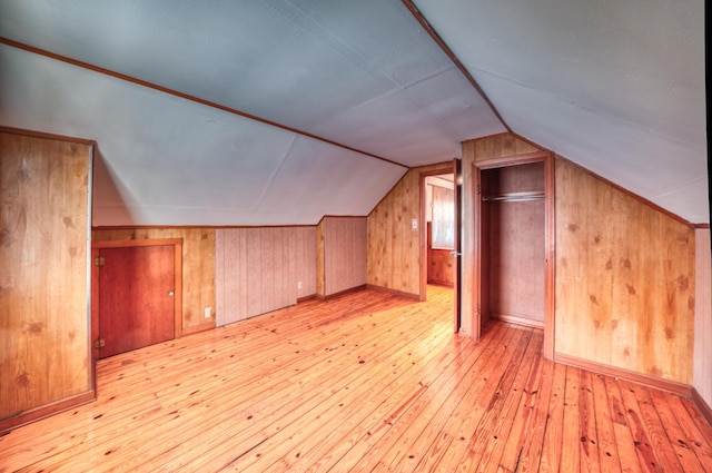 bonus room with lofted ceiling, light wood-style flooring, and wooden walls