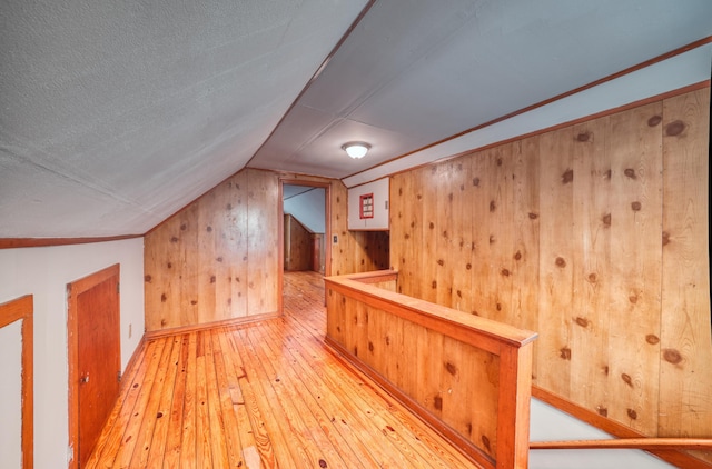 additional living space with wooden walls, a textured ceiling, light wood-style floors, and vaulted ceiling