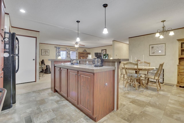 kitchen with a textured ceiling, black refrigerator, ornamental molding, a kitchen island, and pendant lighting