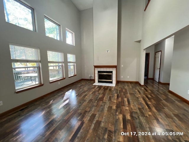 unfurnished living room featuring a fireplace, dark wood-type flooring, and a high ceiling