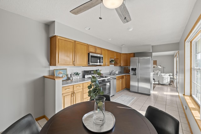 kitchen featuring stainless steel appliances, a textured ceiling, ceiling fan, light tile patterned floors, and sink