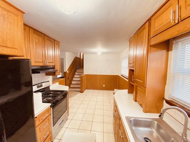 kitchen featuring light tile patterned flooring, stainless steel range with gas cooktop, sink, backsplash, and black fridge