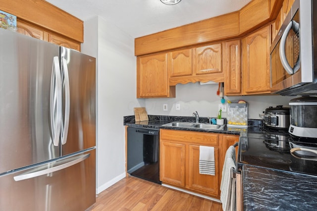 kitchen with stainless steel appliances, sink, dark stone counters, and light hardwood / wood-style flooring