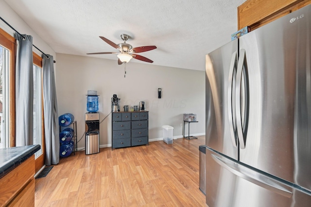 kitchen with ceiling fan, a textured ceiling, stainless steel refrigerator, and light hardwood / wood-style flooring