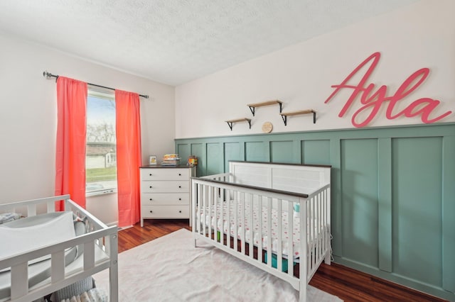 bedroom with a nursery area, dark hardwood / wood-style flooring, and a textured ceiling