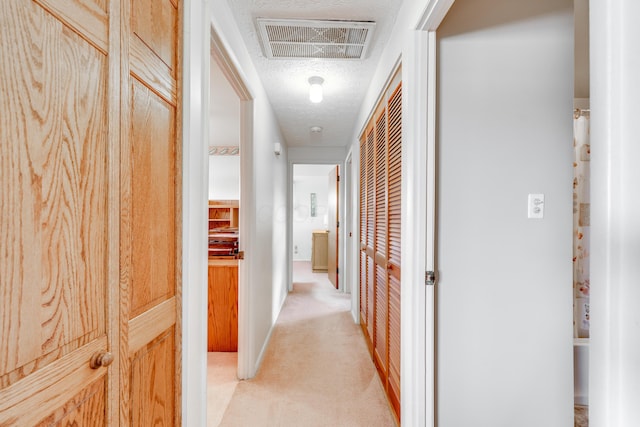 hall with light carpet and a textured ceiling