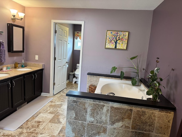 bathroom with vanity, tiled bath, and toilet