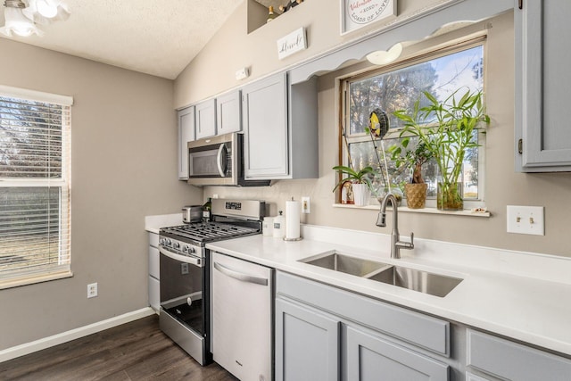 kitchen featuring gray cabinets, vaulted ceiling, sink, stainless steel appliances, and a textured ceiling