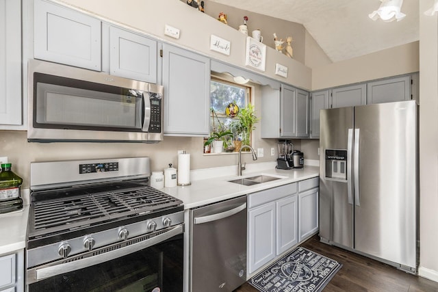 kitchen with sink, gray cabinets, appliances with stainless steel finishes, dark hardwood / wood-style flooring, and vaulted ceiling