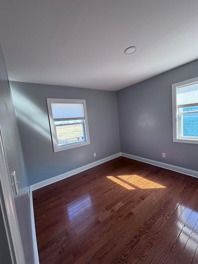 spare room with a wealth of natural light, dark wood-type flooring, and baseboards