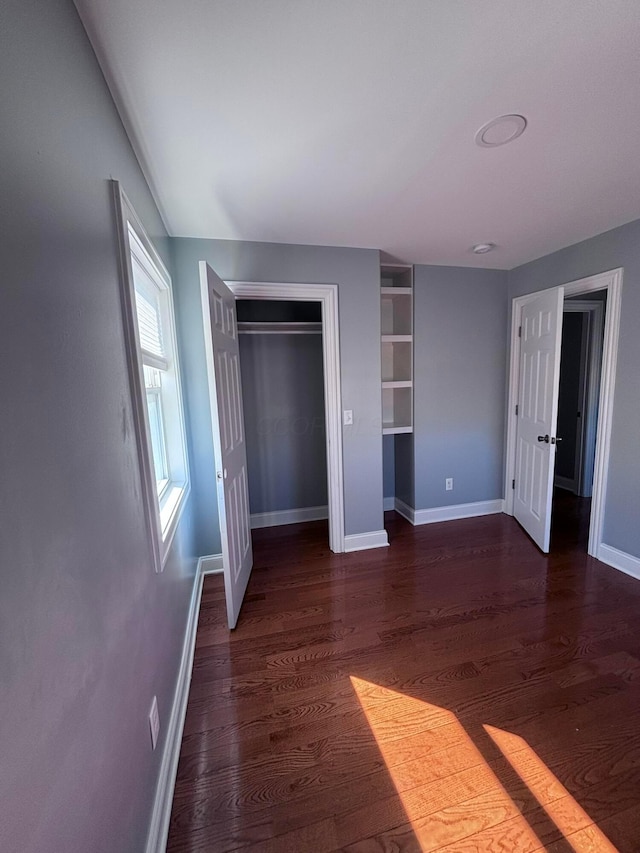 unfurnished bedroom featuring a closet, dark wood-type flooring, and baseboards