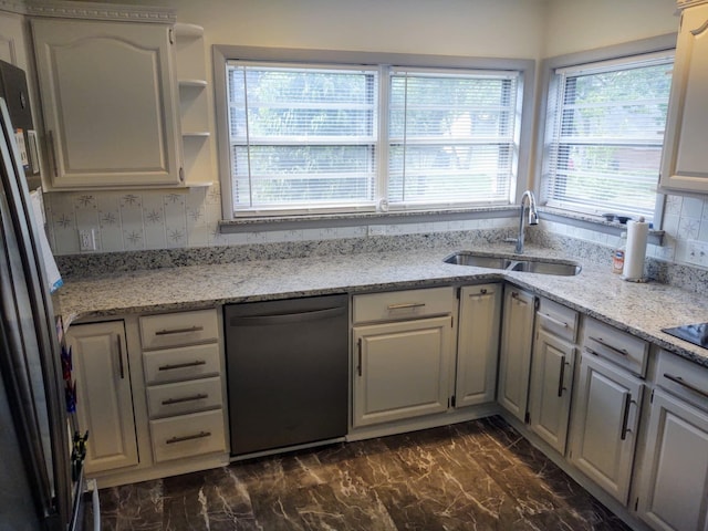 kitchen with sink, tasteful backsplash, stainless steel refrigerator, black dishwasher, and light stone countertops