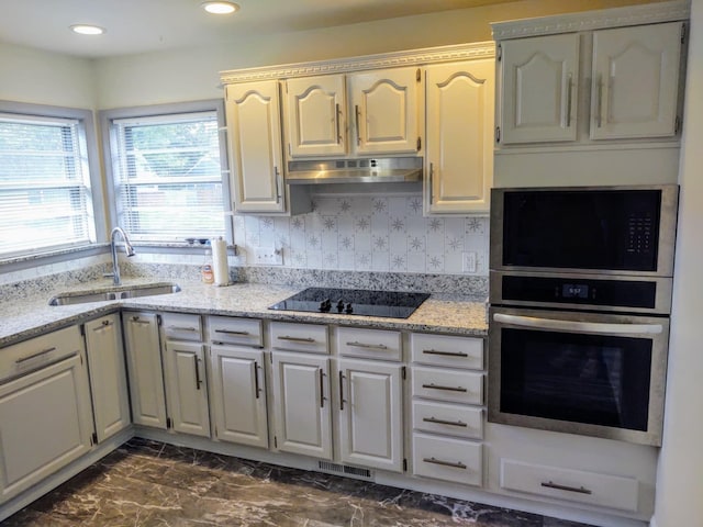 kitchen with black electric stovetop, light stone countertops, sink, and stainless steel oven