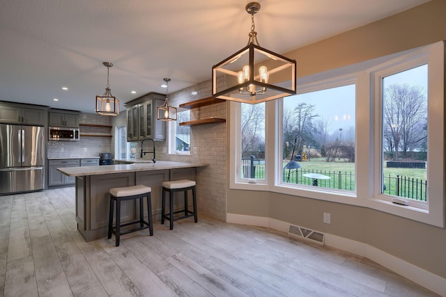 kitchen with sink, appliances with stainless steel finishes, hanging light fixtures, tasteful backsplash, and kitchen peninsula