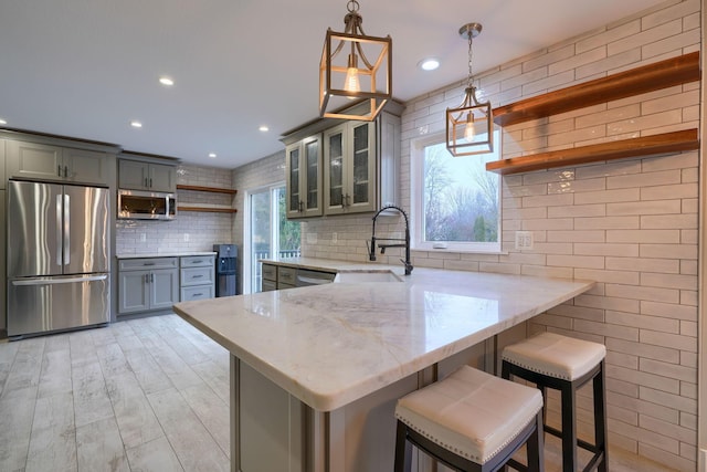 kitchen featuring a breakfast bar, light stone counters, decorative light fixtures, kitchen peninsula, and stainless steel appliances