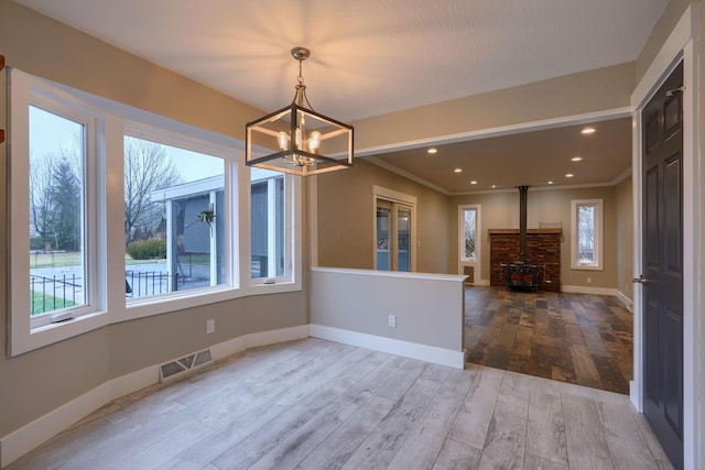 unfurnished dining area with ornamental molding, a wood stove, hardwood / wood-style floors, and a notable chandelier