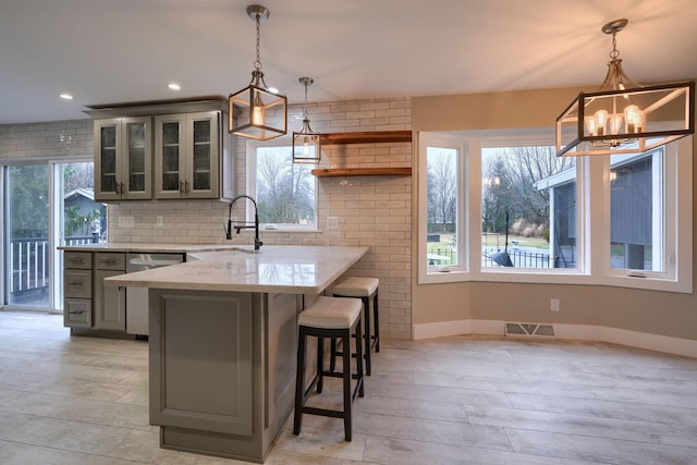 kitchen with sink, gray cabinets, hanging light fixtures, light stone counters, and kitchen peninsula