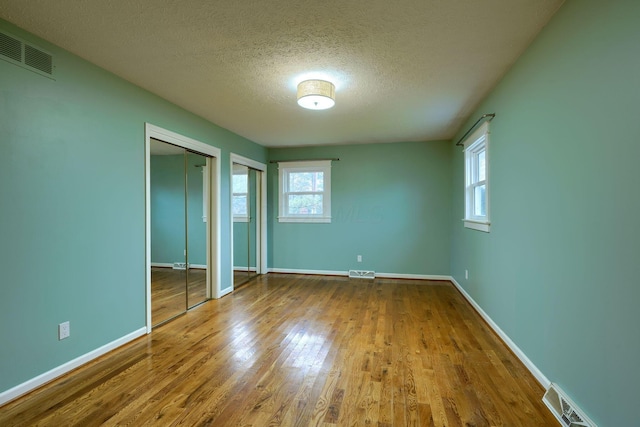 unfurnished bedroom featuring a textured ceiling, wood-type flooring, and multiple closets