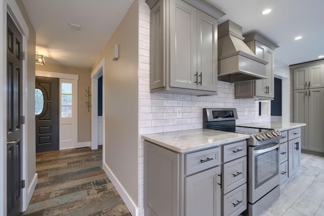 kitchen featuring gray cabinets, light stone counters, custom range hood, decorative backsplash, and stainless steel range with electric cooktop