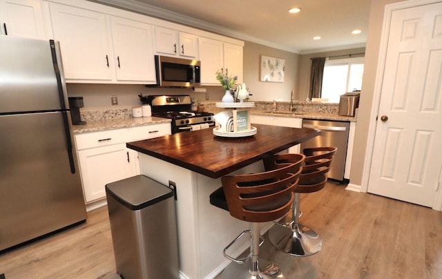 kitchen with white cabinetry, butcher block counters, a center island, stainless steel appliances, and crown molding