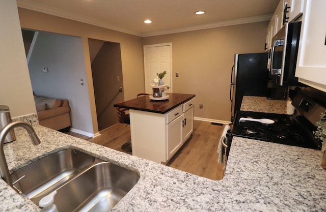 kitchen with appliances with stainless steel finishes, white cabinetry, sink, dark stone countertops, and a center island