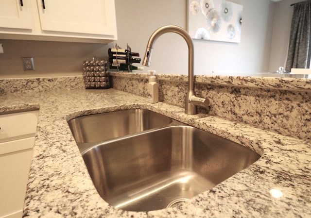 details featuring white cabinetry, light stone countertops, and sink