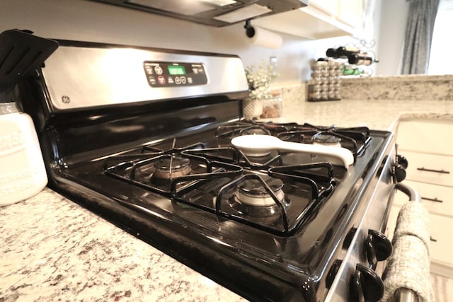 room details with white cabinetry, light stone counters, and gas stove