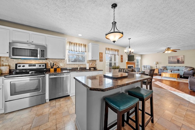 kitchen with tasteful backsplash, hanging light fixtures, a kitchen island, stainless steel appliances, and white cabinets