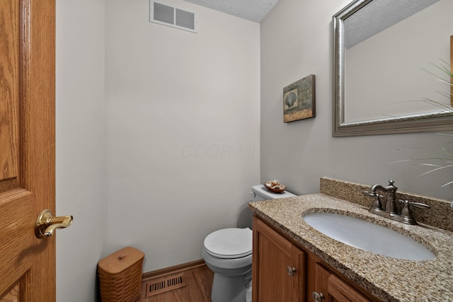 bathroom with hardwood / wood-style flooring, vanity, toilet, and a textured ceiling