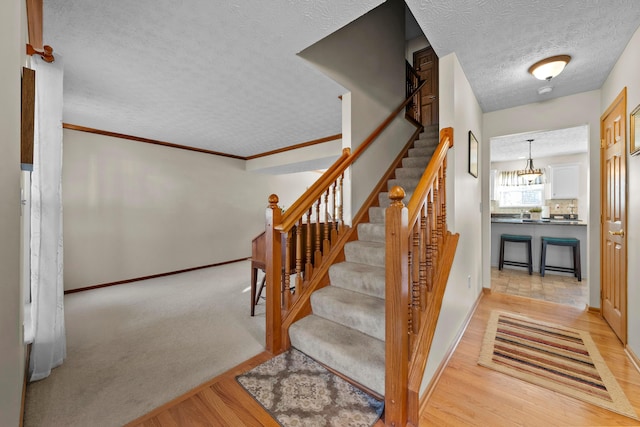 staircase featuring crown molding, hardwood / wood-style flooring, and a textured ceiling