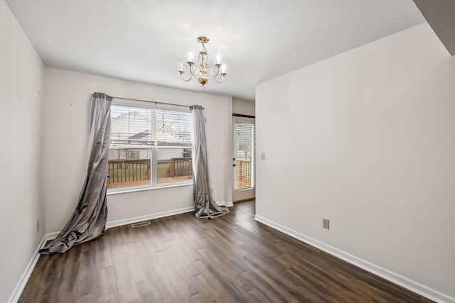 spare room featuring dark wood-type flooring and a chandelier